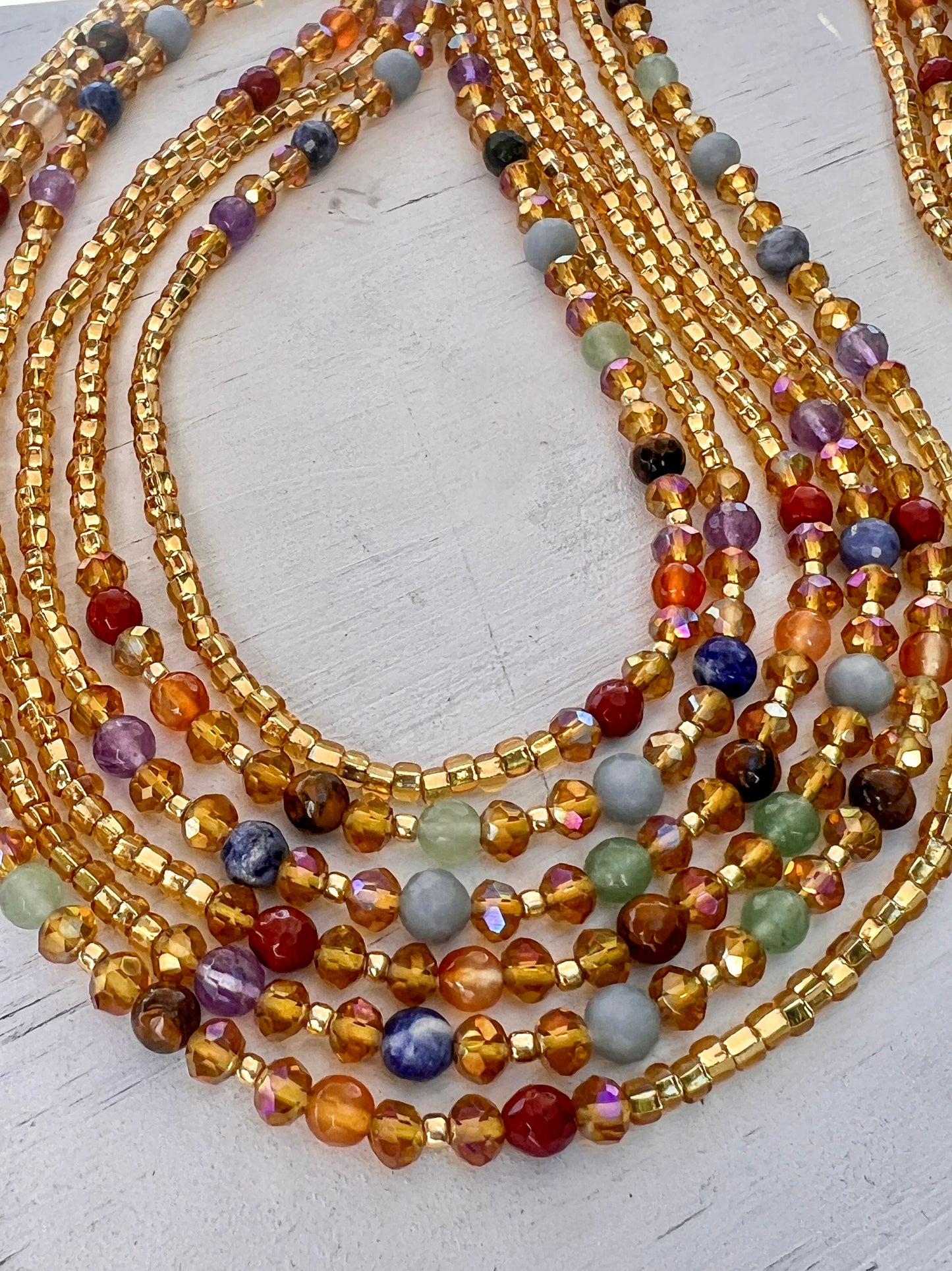 Gold waist beads with shimmering seed beads and multicolored gemstones, handcrafted by Sia Body Beads.