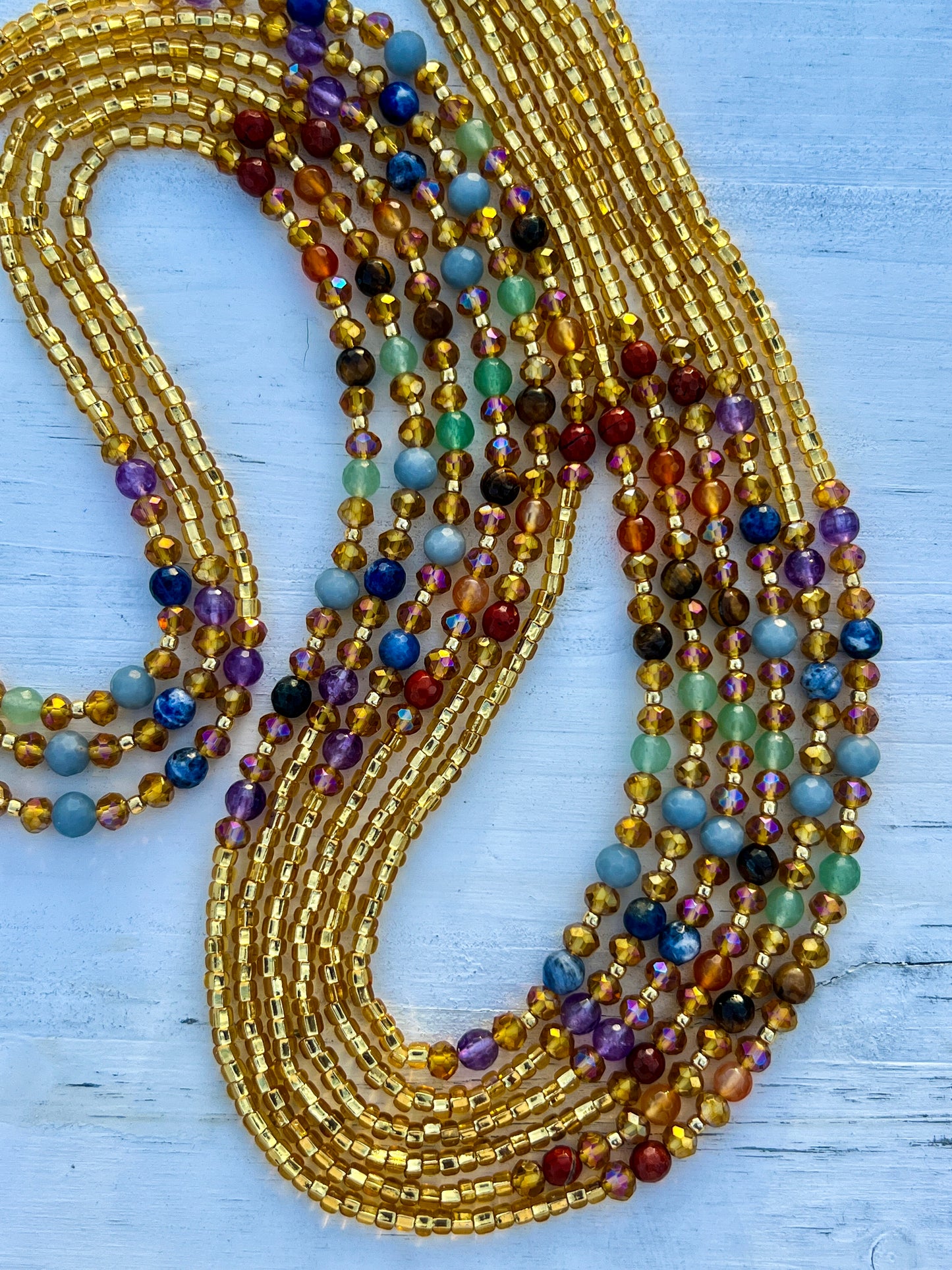 Gold waist beads with shimmering seed beads and multicolored gemstones, handcrafted by Sia Body Beads.
