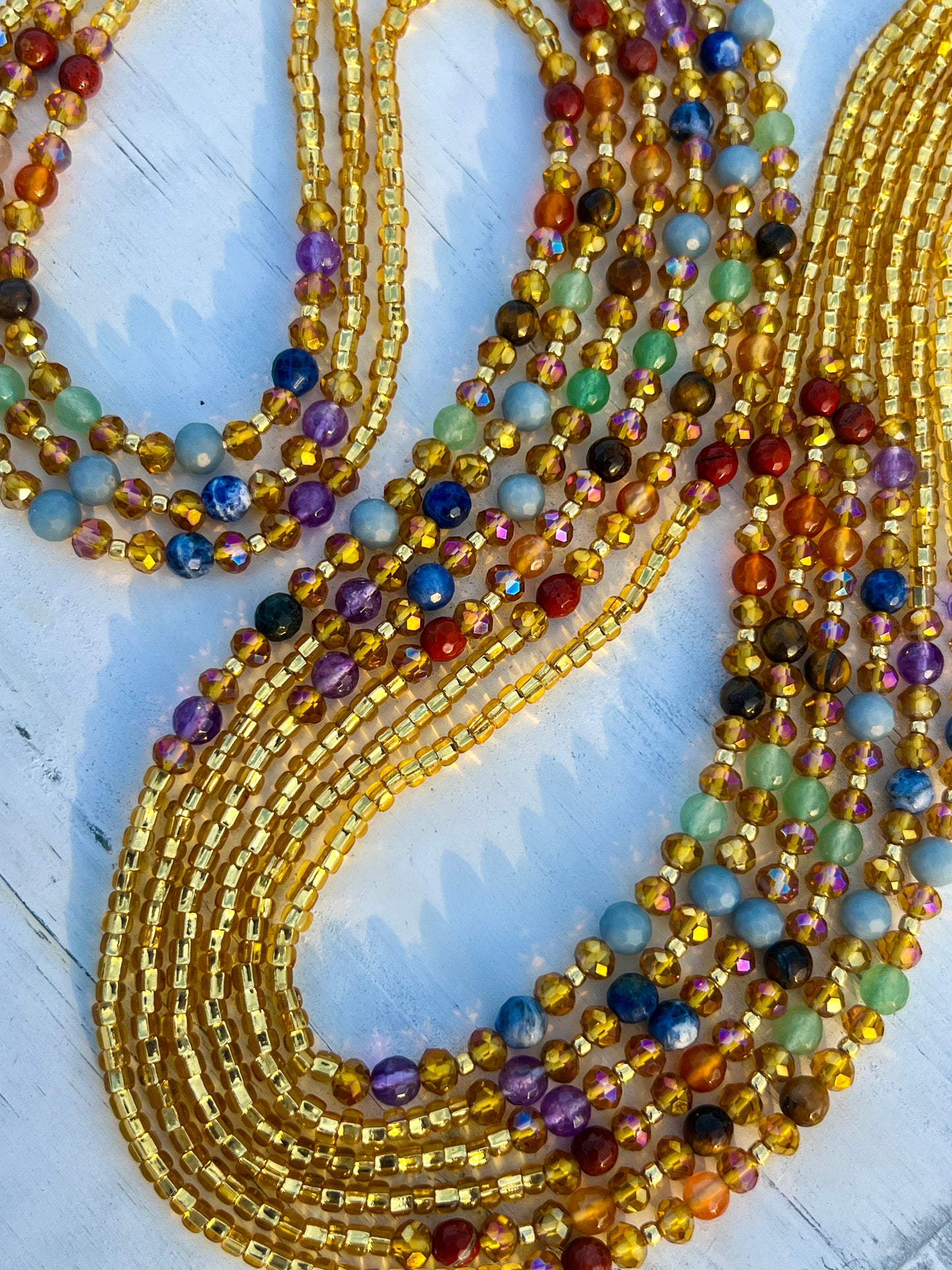 Gold waist beads with shimmering seed beads and multicolored gemstones, handcrafted by Sia Body Beads.