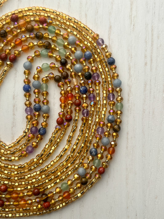 Gold waist beads with shimmering seed beads and multicolored gemstones, handcrafted by Sia Body Beads.