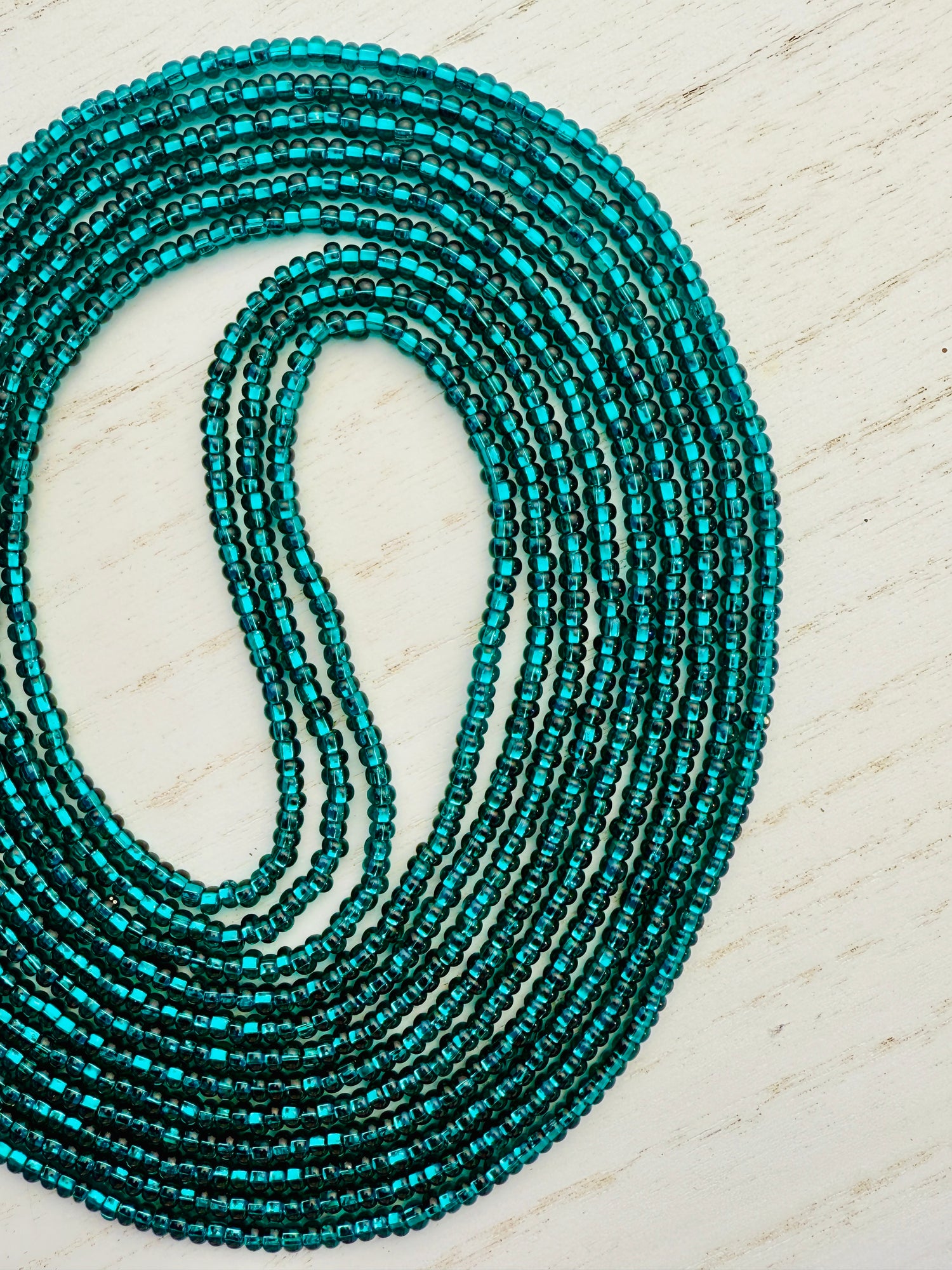 Emerald green glass waist beads on a light wooden surface