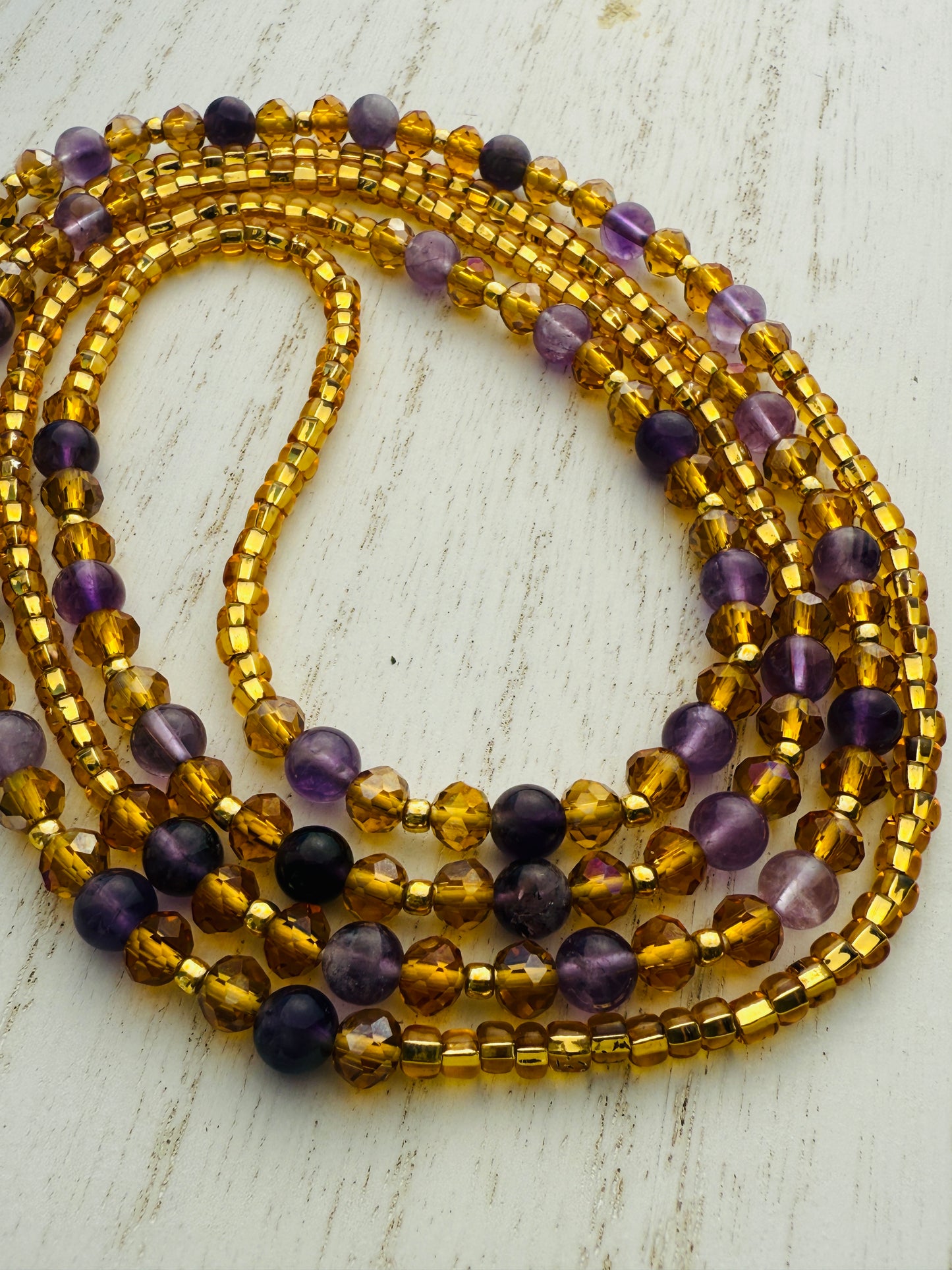 Stack of gold and purple waist beads on a light wooden surface