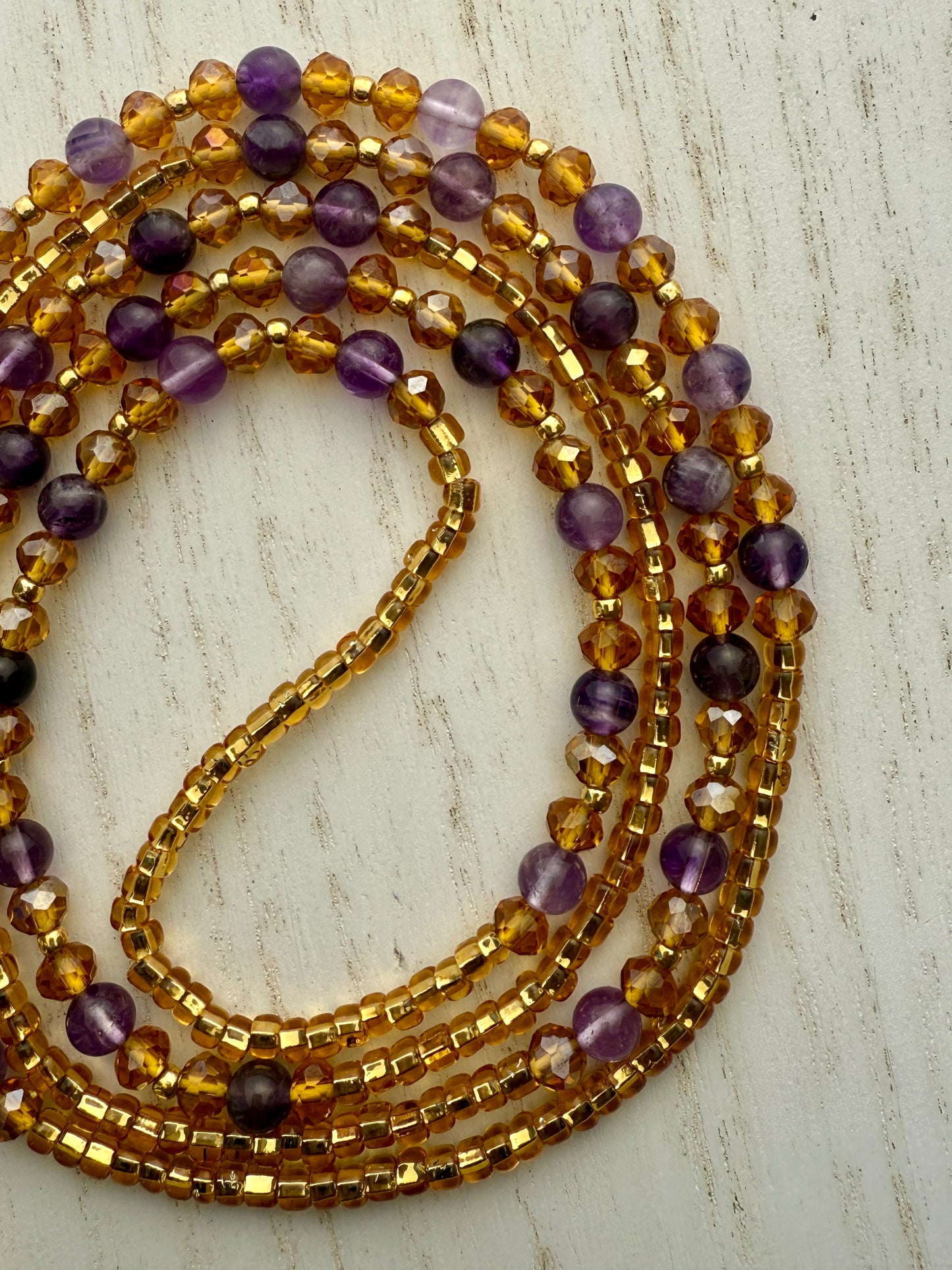Stack of gold and purple waist beads on a light wooden surface
