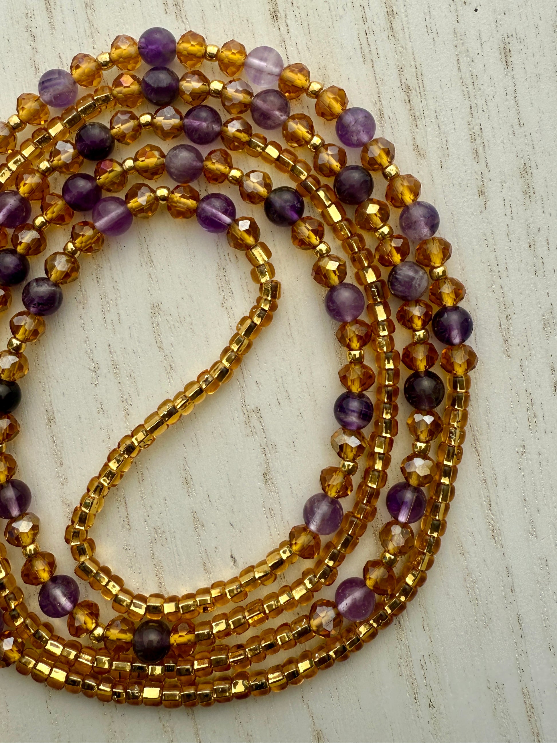 Stack of gold and purple waist beads on a light wooden surface