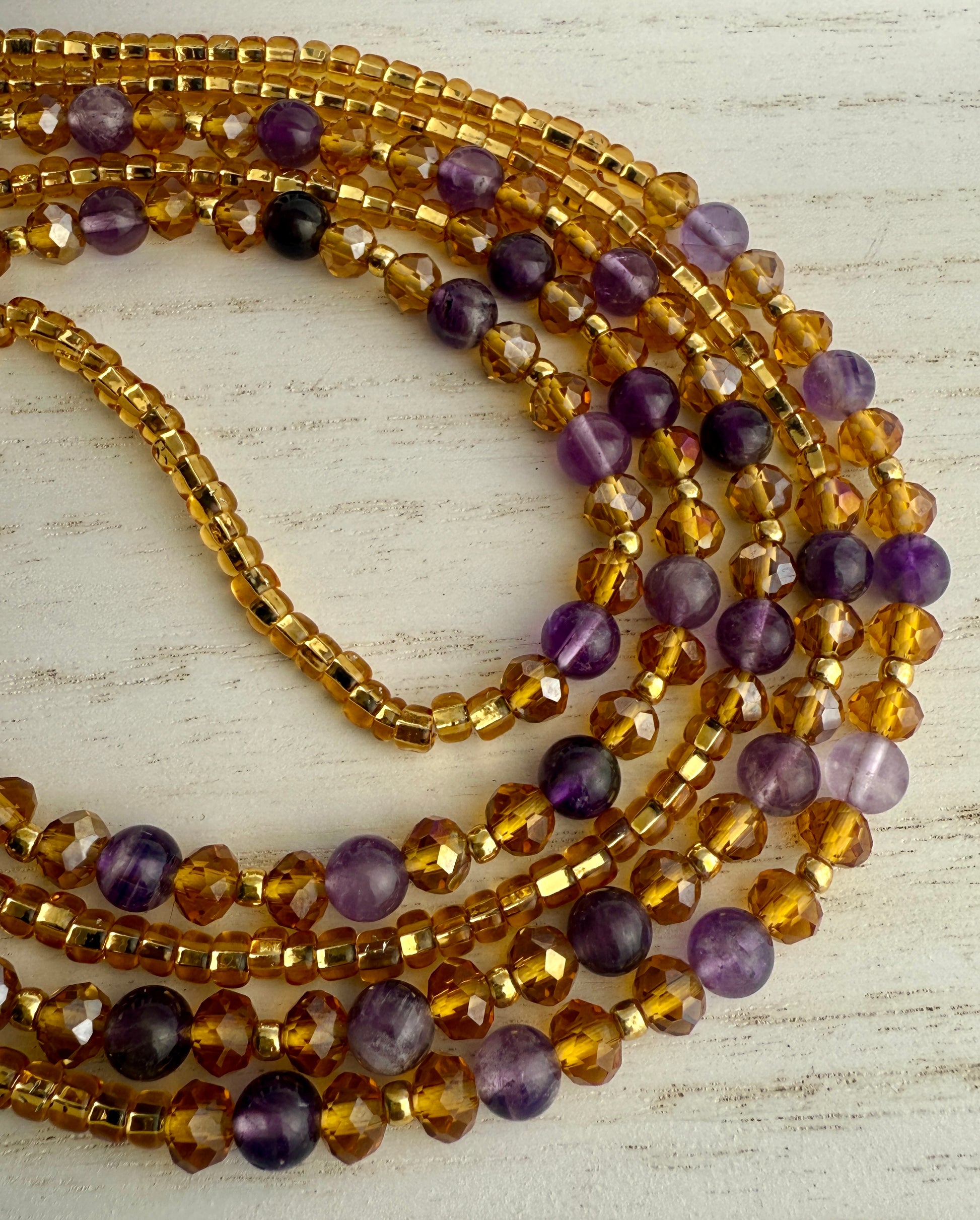 Stack of gold and purple waist beads on a light wooden surface