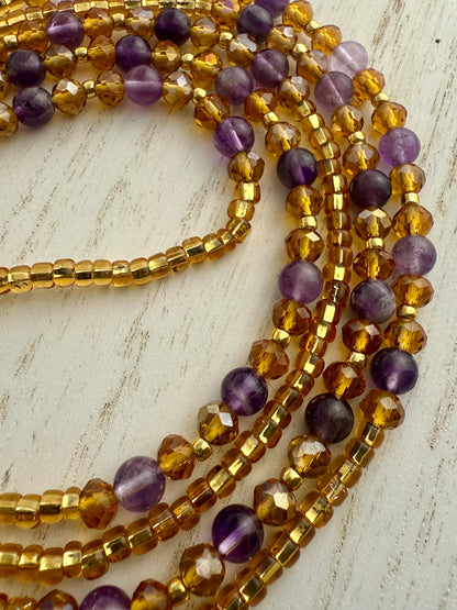 Stack of gold and purple waist beads on a light wooden surface