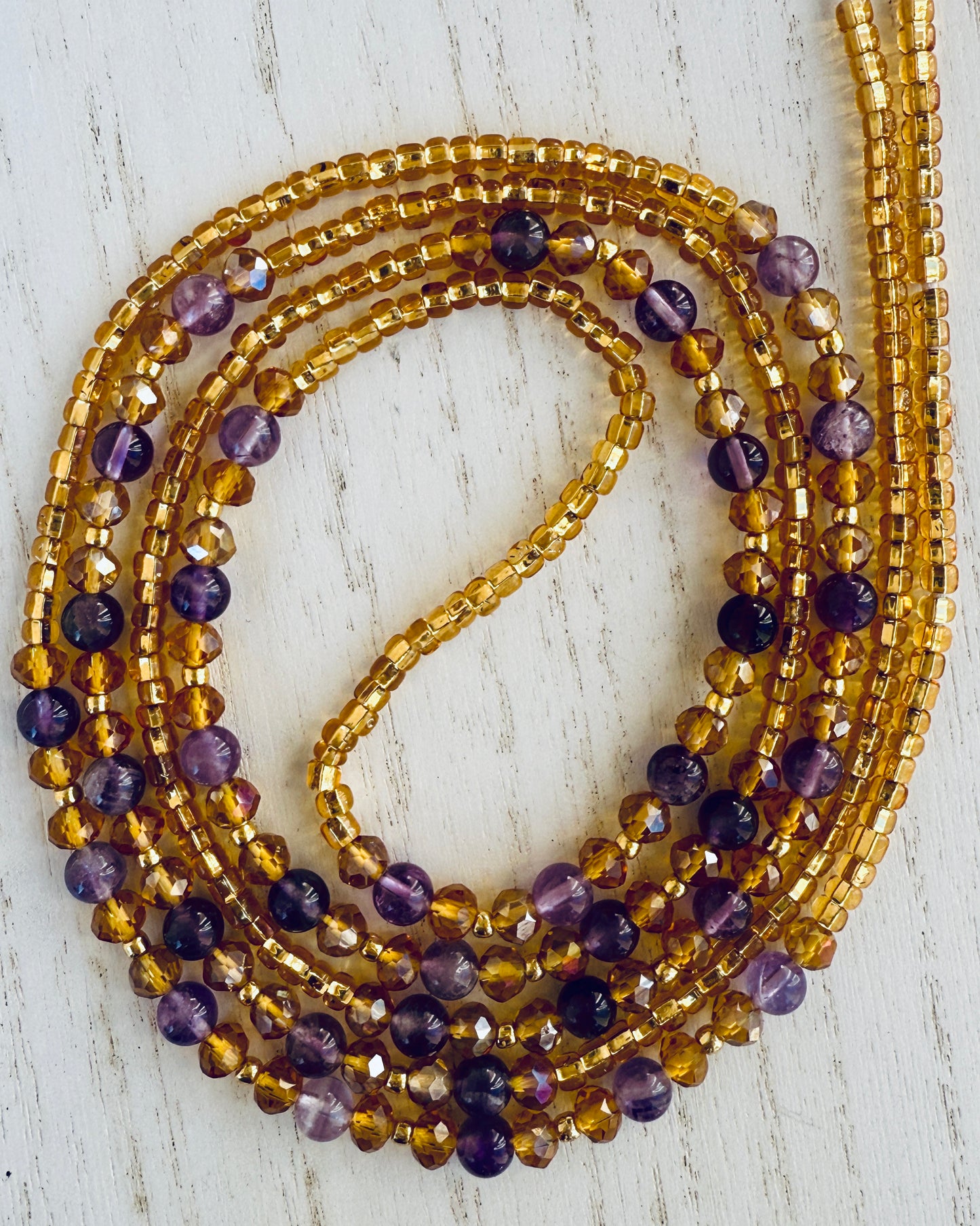Stack of gold and purple waist beads on a light wooden surface