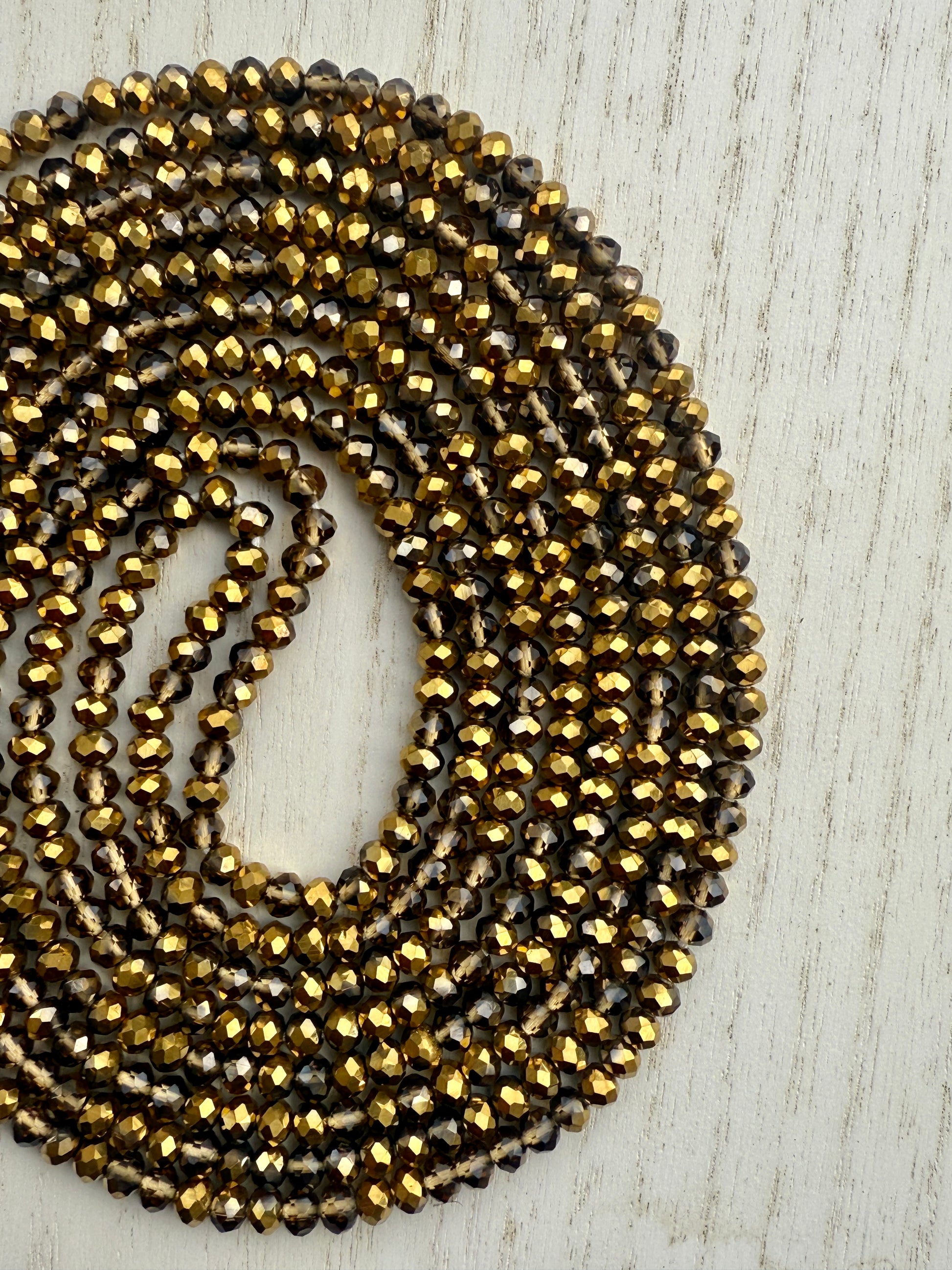 gold and bronze faceted crystal waist beads displayed in a circle on a neutral textured surface