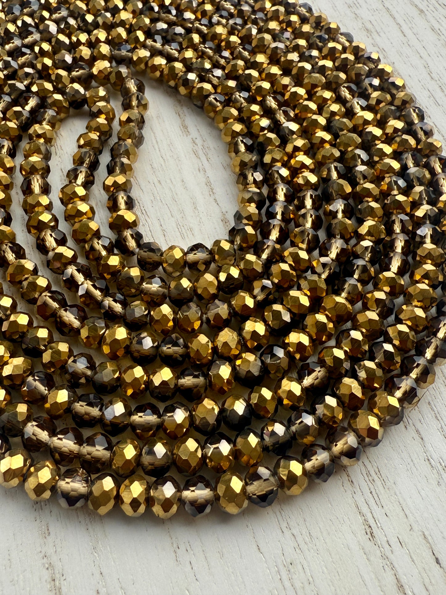gold and bronze faceted crystal waist beads displayed in a circle on a neutral textured surface