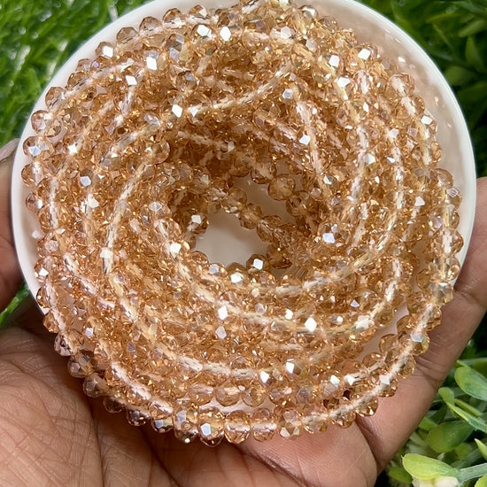 Rose gold waist beads made with faceted beads, coiled in a circular container on a grassy background.