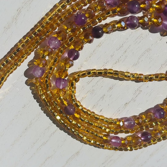 Stack of gold and purple waist beads on a light wooden surface