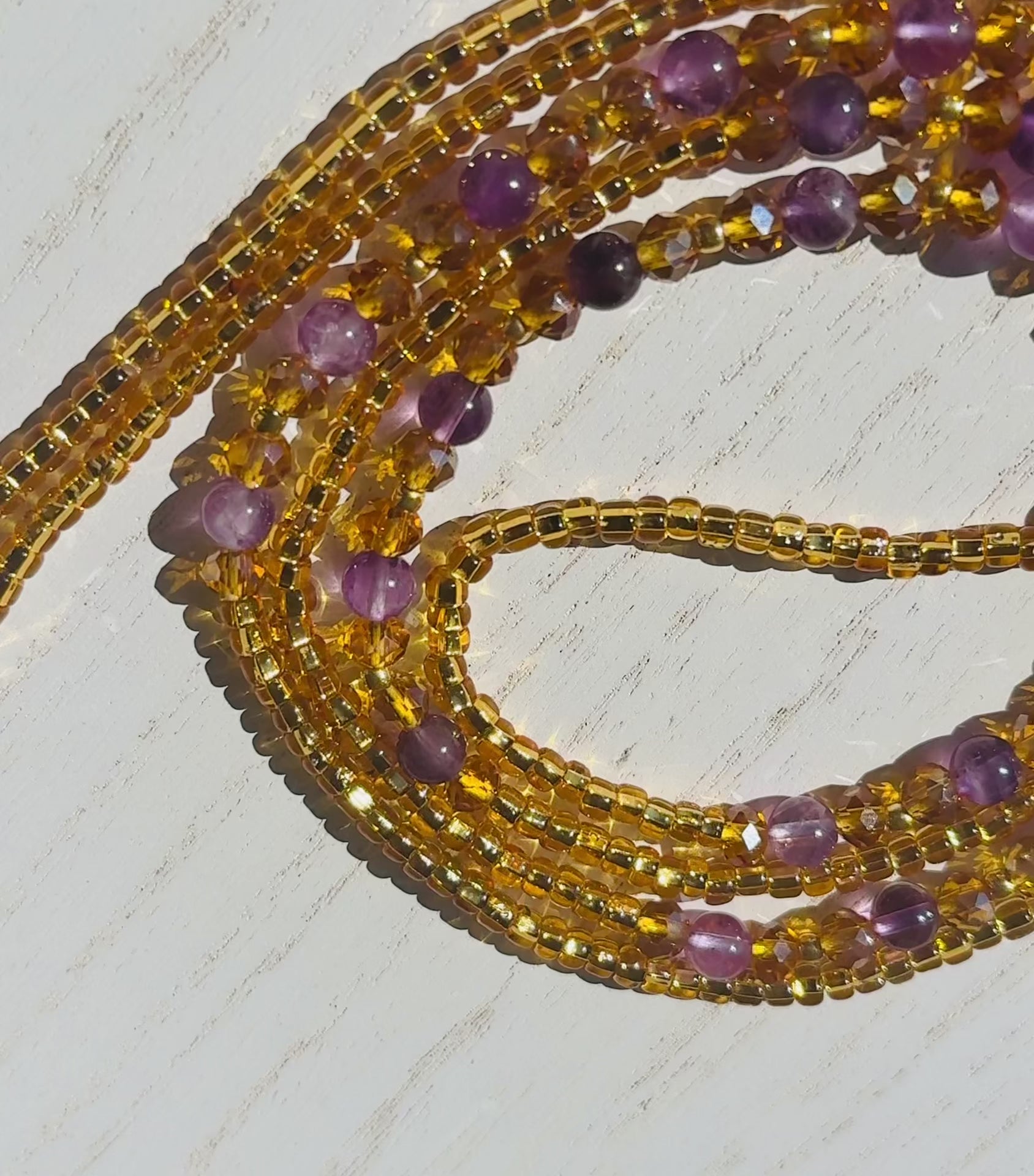 Stack of gold and purple waist beads on a light wooden surface