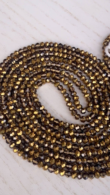 gold and bronze faceted crystal waist beads displayed in a circle on a neutral textured surface
